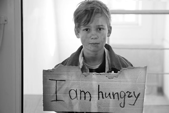 Homeless little boy begging for food, view through glass door