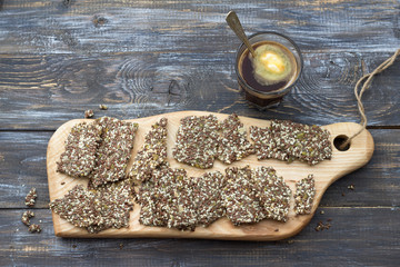 Delicious healthy multigrain gluten-free crackers, ketogenic, from chia seeds, flax, sesame and ground pumpkin seeds on wooden board and keto coffee in glass with spoon of butter оn wooden table	