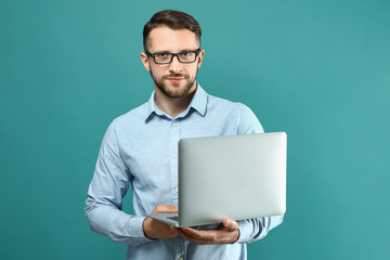 Handsome man with laptop on color background