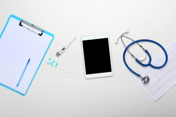 Clipboard, tablet computer, stethoscope and pills on white background