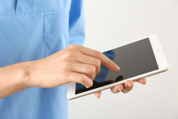 Nurse with tablet computer on light background, closeup