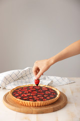 Woman decorating tasty chocolate cake with strawberry on table