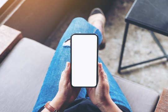 Top view mockup image of woman holding black mobile phone with blank screen while sitting in cafe