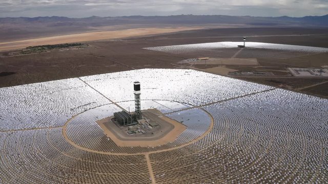 Awesome aerial flight over two power stations with towers in the middle of solar panels circles. Mirrors glare with silver light in brown dry dusty desert. Aerial 4K