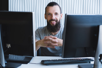 Successful professional career. Cheerful male web designer sitting at his workplace, smiling.