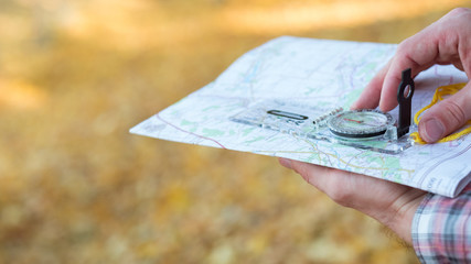 Traveler lifestyle. Closeup of man hands holding compass and map. Blur yellow grass background....