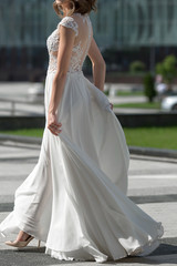 Fototapeta na wymiar light airy wedding dress with a slit for the legs. The bride walks in a simple elegant wedding dress. White dress with a high slit flutters in the wind during a walk.