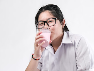 Happy Asian student in uniform drinking strawberry milk in glass on white background.