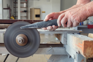 Hands of worker wich is sharpering knife on grindstone