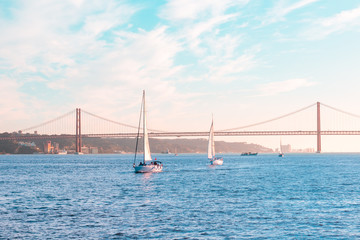 Fototapeta na wymiar Sailing boats floating on the sea Bay against the backdrop of a large iron bridge, blue sky and sunset