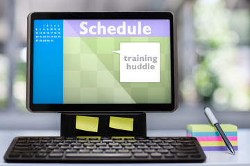 A tablet computer workstation with mockup scheduling software application on a office desk with colorful sticky notes, a pen and wireless keyboard.