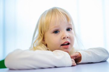 Little girl listening to female teacher in school classroom. Happy smiling pupil