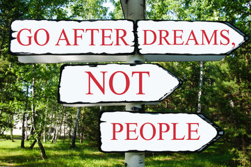 Motivational expression on signpost "GO AFTER DREAMS NOT PEOPLE" against the background of green forest. 
