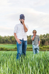 Naklejka na ściany i meble Two men in plaid shirt standing in oat field with forest in background posing