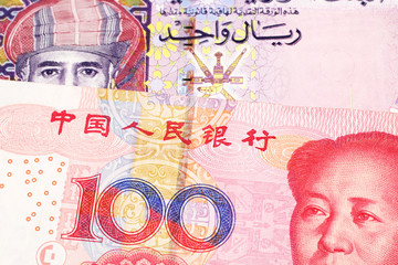 A multicolored one rial note from Oman, close up in macro with a red, Chinese one hundred yuan renminbi bill