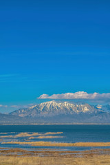 Vivid blue sky with puffy clouds over a snow peaked mountain and calm lake