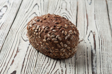 One whole loaf of rye bread with seeds of sunflower lies on old weathered white wooden table