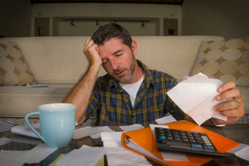 frustrated man at home living room couch doing domestic accounting overwhelmed and worried suffering financial problem going over taxes and payments paperwork