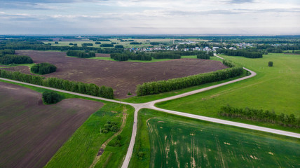 Aerial shot. Amazing view of the crossroads of rural road among the fields. On cloudy summer day