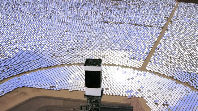 Drone flight around power tower rounded with lots of solar panels that reflects violet sky and shines bright. Aerial 4K