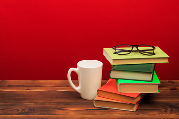 pile of books with glasses and mug on red background 