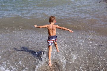 Fototapeta premium active little sport kid in shorts running into waves of ocean on summer beach
