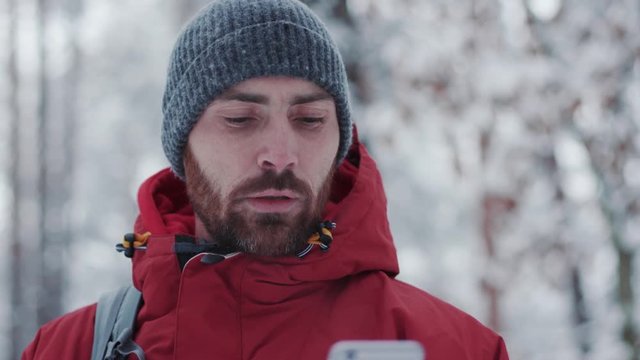 Young man traveler using smart phone in winter forest adventure cold jacket mobile nature phone tourist trip adult caucasian cell communication landscape slow motion