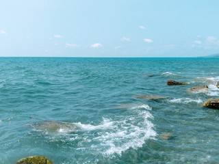 abstract background of bright turquoise sea water, under the water a huge concrete stones as the breakers, the white foam of the surf, the sunlight sparkle on the ocean waves, a strip of azure sky