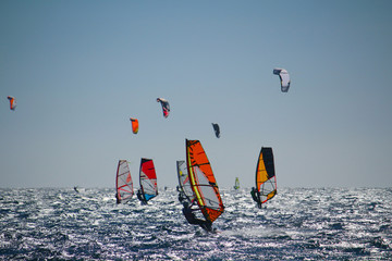 Windsurfers and kiteboarders on choppy sea, in backlight