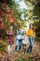 Fototapeta premium A group of four children in the autumn forest. Children are holding maple leaves and smiling happily