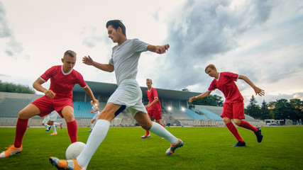 Professional Soccer Player Leads with a Ball, Masterfully Dribbling and Bypassing Sliding Tackles of His Opponents. Two Professional Football Teams Playing. Low Angle Shot.