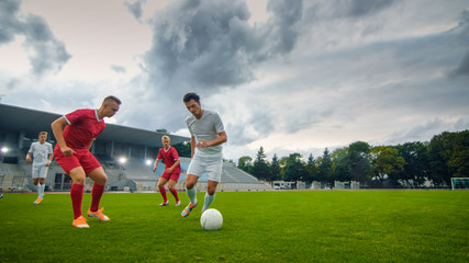 Professional Soccer Player Leads with a Ball, Masterfully Dribbling and Bypassing Sliding Tackles of His Opponents. Two Professional Football Teams Playing. Low Angle Shot.