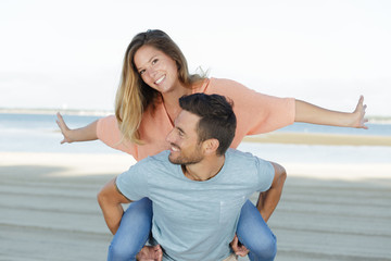 man giving piggyback ride to girlfriend by the ocean