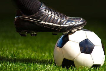 Football soccer player foot with a soccer ball on a field with green grass