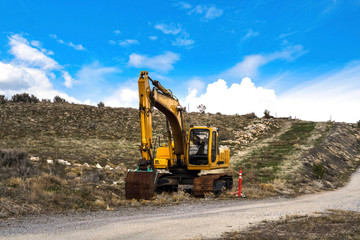 Yellow excavator and orange traffic delineator post beside a mountain road
