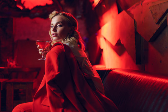 Image of young blonde woman in red jacket with cocktail in her hand in nightclub