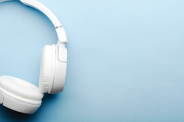 White overhead wireless bluetooth headphones on a blue background. Close-up, copy space, top view,...