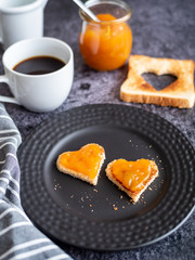 Toastbrot mit Aprikosenkonfitüre in Herzform auf einem grauen Teller, Frühstück, Kaffee