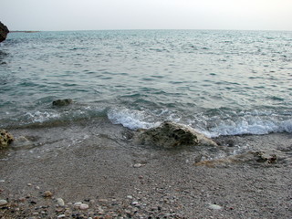 The landscape of the sea coast is tiled with a small pebble soaked by gentle waves against the background of the boundless ocean.