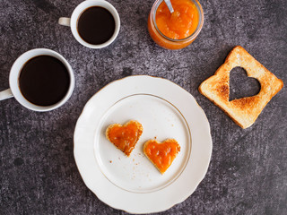 Kaffee und Toastbrot mit Aprikosenkonfitür in Herzform auf einem weißen Teller, Draufsicht, Frühstück