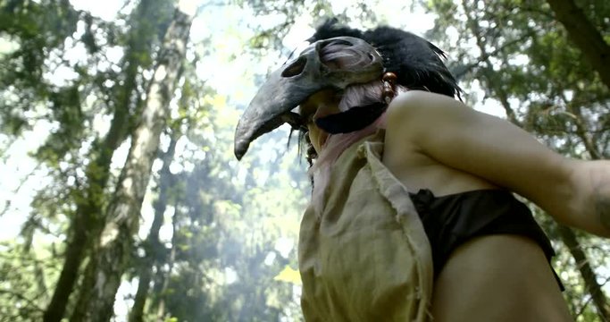 crazy savage female witch is moving in forest in daytime, view on her face with mask