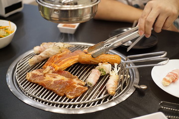 A man grilling porks ,hotdog, Glazed Pork and Vegetable on Charcoal grilled Korean-Style BBQ.