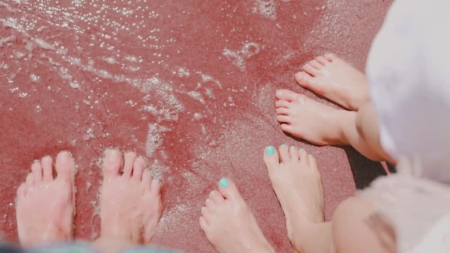 he waves wash the feet of the man and the feet of the woman and the feet of the child on the dark red sand by the sea Kokkini Paralia, Santorini, Greece, relaxation, family vacation, trip