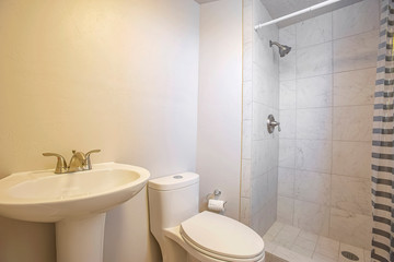 Stand alone sink toilet and shower inside a small bathrrom with white wall