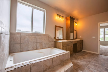 Built in bathtub in front the window of a bathroom with tiled floor and wall