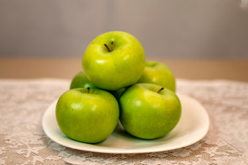 Green apples served on white porcelain plate on a table covered with white lace towel.