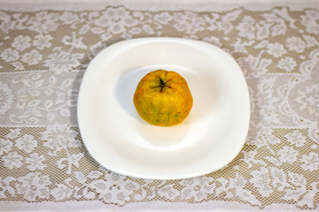 Tangerine served in white porcelain dish on a table covered with white lace towel.