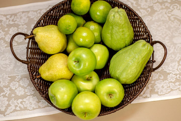  Fruits and vegetables of green color inside basket brown on white lace tablecloth.