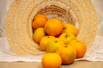 Tangerines served in female straw hat, on the table and white lace towel.