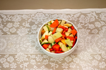Raw vegetables in white bowl, chopped over white lace towel.